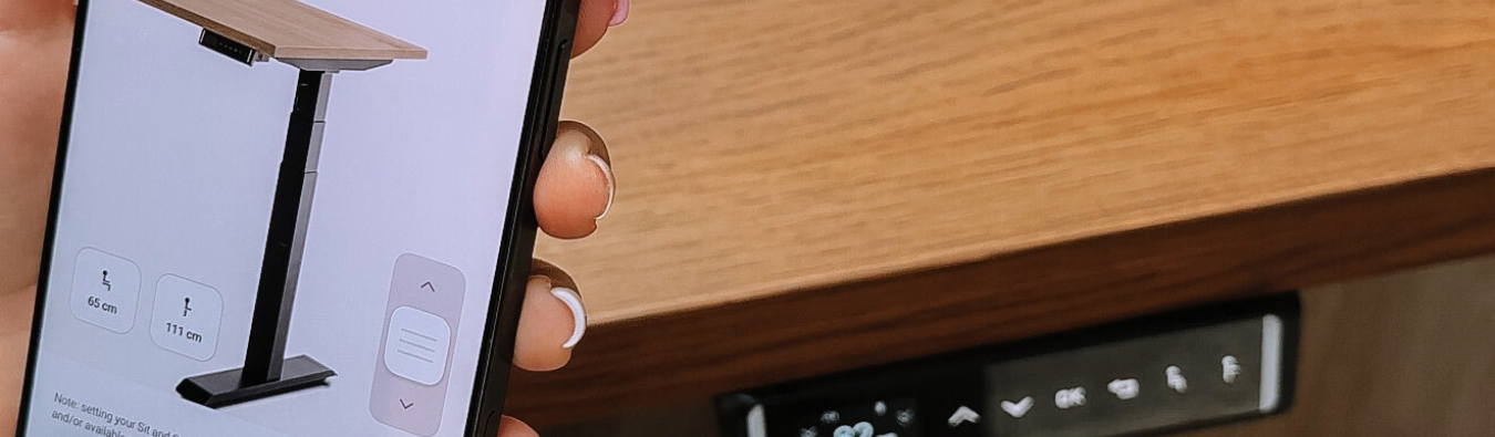 Person using a smartphone to control a standing desk with a wooden surface.