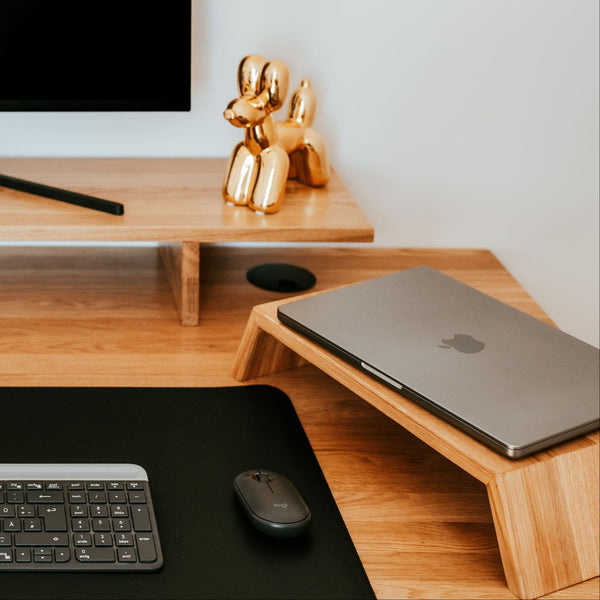 Stehpult aus massiver europäischer Eiche mit integriertem Monitorhalter und Laptopständer aus Eiche, ausgestattet mit einer schwarzen Schreibtischunterlage, einer Tastatur und Maus von Logitech sowie goldenen Ballonhund-Dekorationen – modernes skandinavisches Homeoffice
