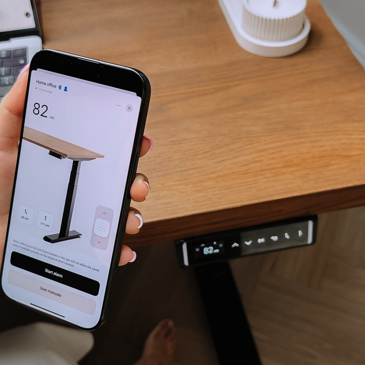 Person using a smartphone to control a standing desk with a wooden surface.
