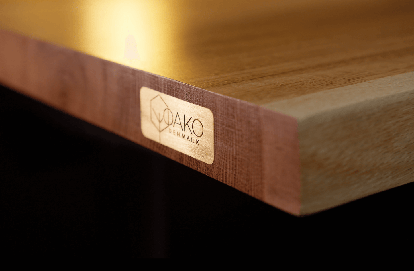 Close-up of the OAKO Denmark logo engraved on a solid oak desk, highlighting the premium craftsmanship and natural wood quality. Ideal for showcasing the brand's dedication to sustainable and ergonomic furniture design.