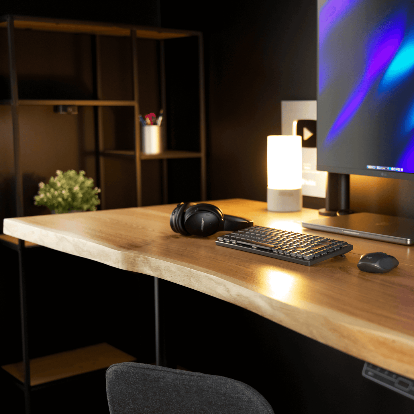 Close-up view of OAKO Denmark's natural oak desk in a modern workspace setup, featuring a live edge wooden surface paired with black metal legs. The desk is accessorized with a keyboard, mouse, headphones, and a stylish lamp, creating a cozy and productive environment.